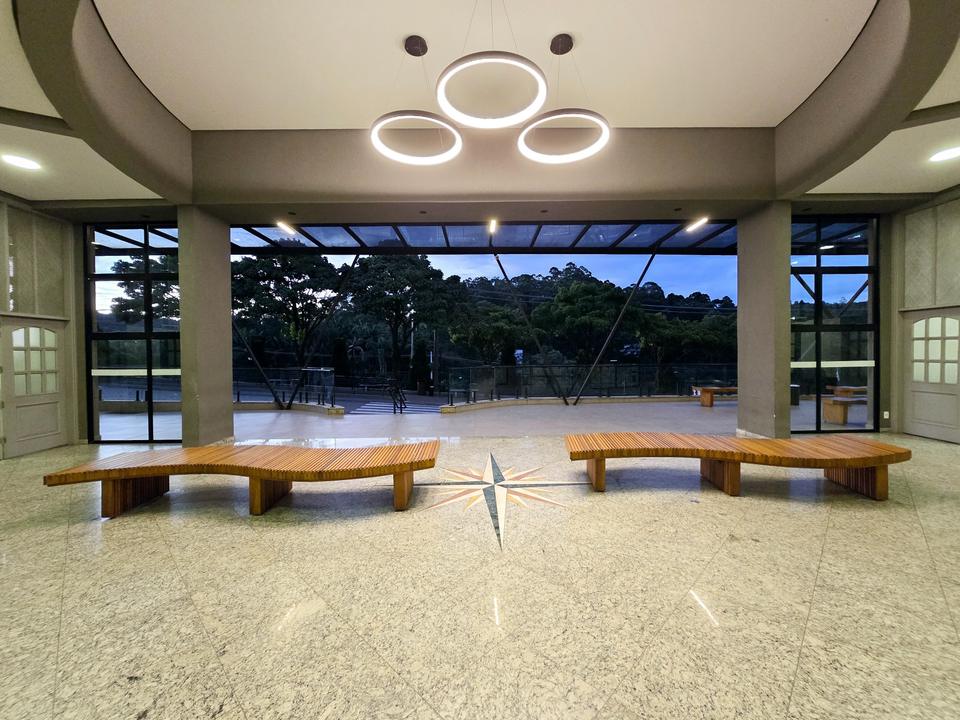 Hall interno iluminado, com bancos de madeira e vista para o jardim